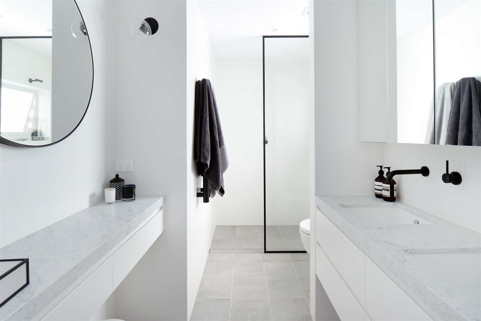 This is an example of a mid-sized contemporary 3/4 bathroom in Sydney with flat-panel cabinets, white cabinets, a two-piece toilet, white tile, ceramic tile, white walls, ceramic floors, a wall-mount sink, solid surface benchtops, grey floor, an open shower and white benchtops.