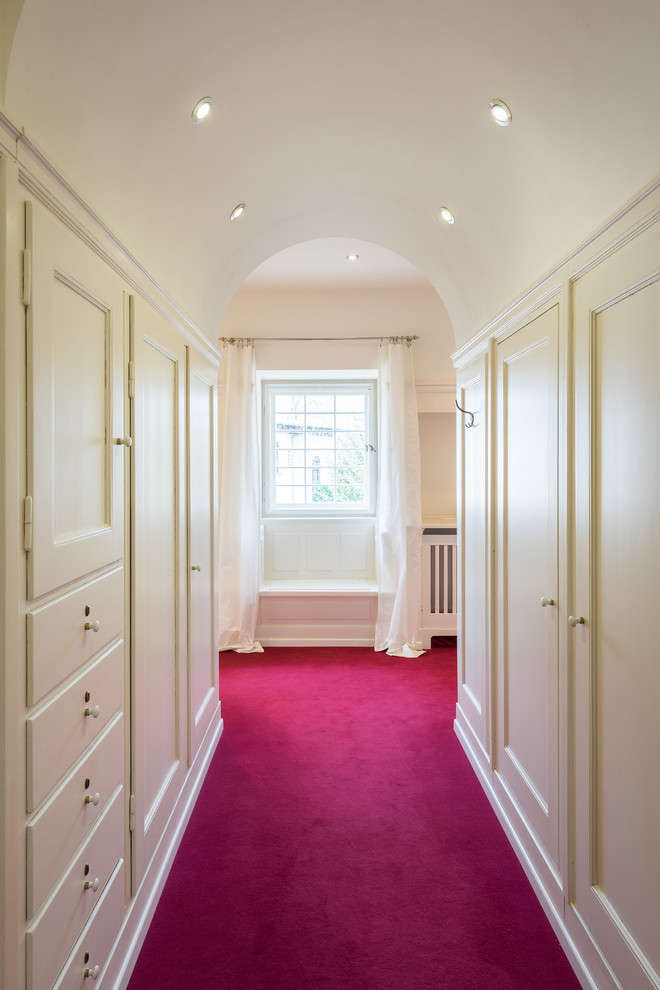 Design ideas for a mid-sized traditional women's built-in wardrobe in Leipzig with recessed-panel cabinets, white cabinets, carpet and pink floor.