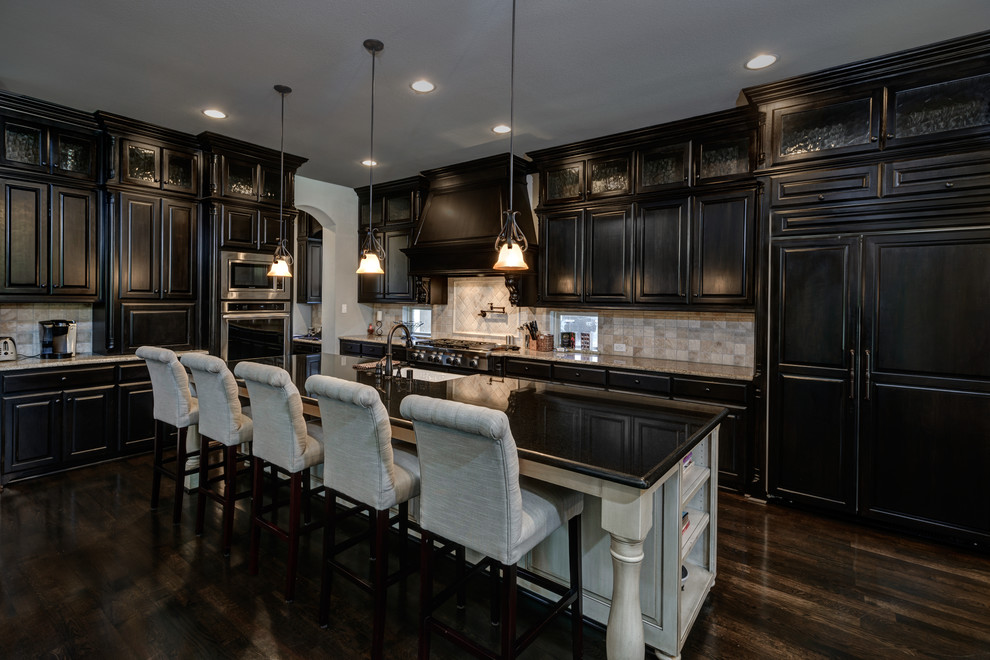 Photo of a large transitional l-shaped eat-in kitchen in Dallas with an undermount sink, recessed-panel cabinets, black cabinets, granite benchtops, beige splashback, stone tile splashback, stainless steel appliances, dark hardwood floors, with island and brown floor.