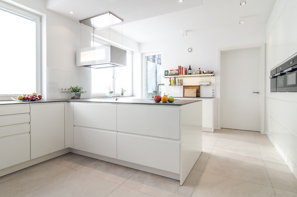 Photo of a mid-sized contemporary l-shaped separate kitchen in Frankfurt with flat-panel cabinets, white cabinets, white splashback, glass sheet splashback, black appliances, a peninsula and beige floor.