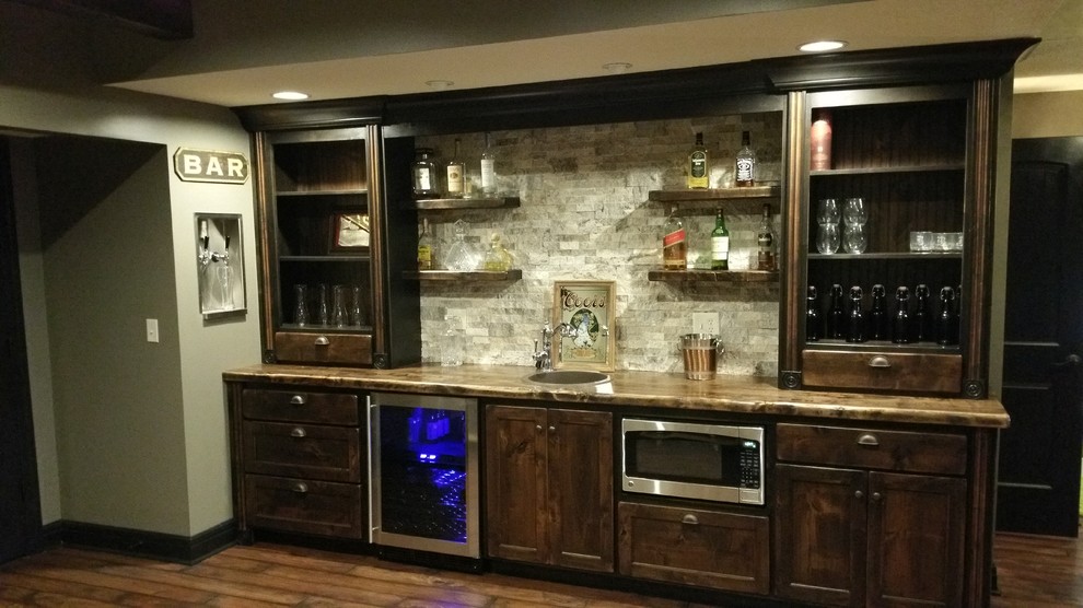 Photo of a mid-sized arts and crafts single-wall wet bar in Kansas City with a drop-in sink, shaker cabinets, dark wood cabinets, grey splashback, stone tile splashback, medium hardwood floors and brown floor.