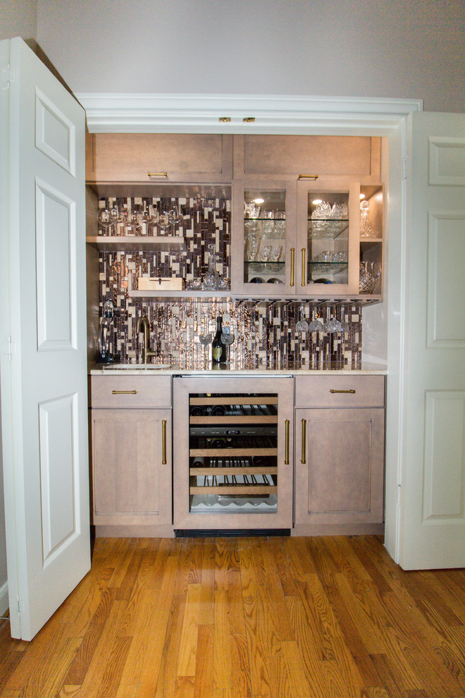 This is an example of a small contemporary single-wall wet bar in Houston with an undermount sink, shaker cabinets, beige cabinets, marble benchtops, brown splashback, glass tile splashback, light hardwood floors and brown floor.