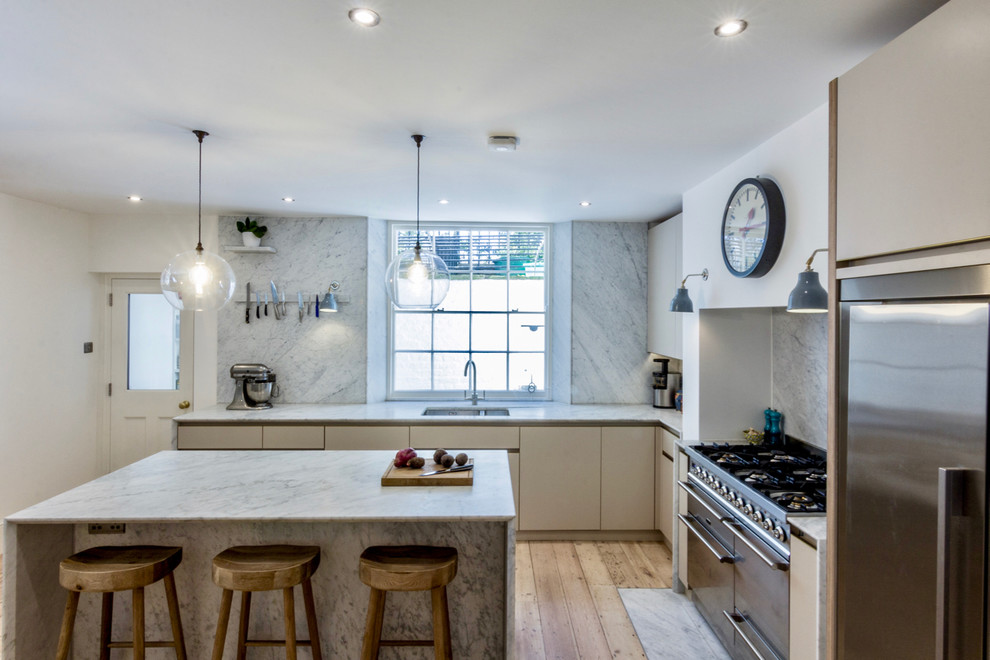Inspiration for a large contemporary l-shaped kitchen in London with a double-bowl sink, flat-panel cabinets, beige cabinets, marble benchtops, white splashback, marble splashback, stainless steel appliances, light hardwood floors, with island, beige floor and white benchtop.