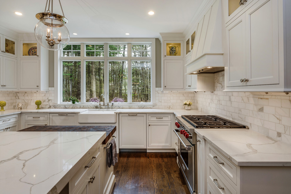 Example of a large transitional u-shaped dark wood floor and brown floor kitchen design in Bridgeport with a farmhouse sink, flat-panel cabinets, white cabinets, quartz countertops, white backsplash, marble backsplash, stainless steel appliances, an island and white countertops