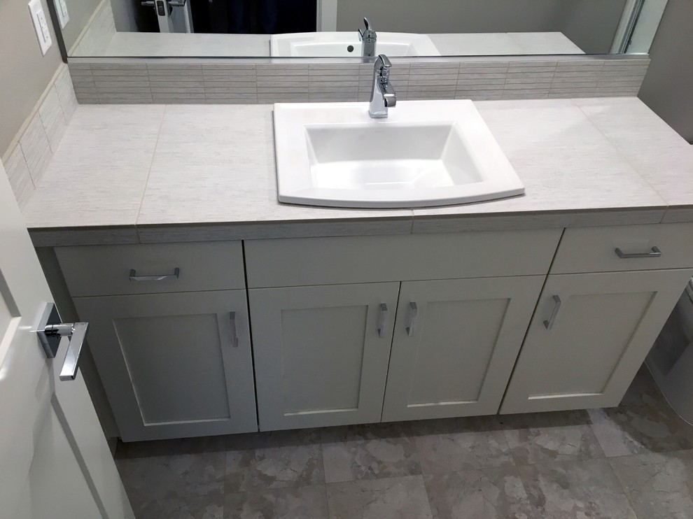 3/4 bathroom in Portland with shaker cabinets, white cabinets, gray tile, ceramic tile, grey walls, linoleum floors, a drop-in sink, tile benchtops, grey floor and grey benchtops.