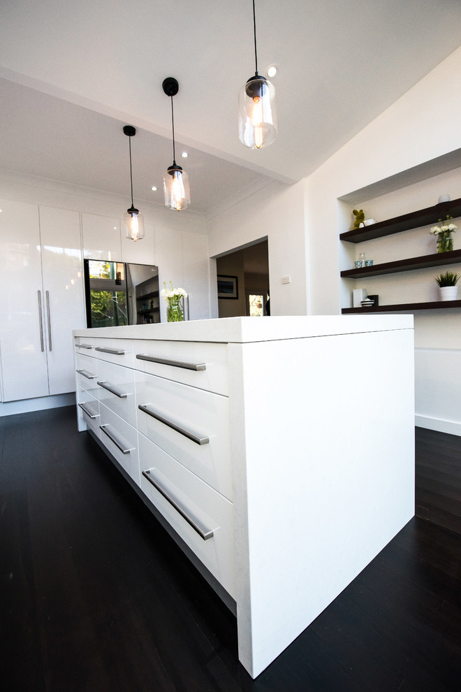 Mid-sized contemporary l-shaped eat-in kitchen in Sydney with flat-panel cabinets, white cabinets, quartz benchtops, black splashback, with island, an undermount sink, porcelain splashback, stainless steel appliances, dark hardwood floors, black floor and white benchtop.