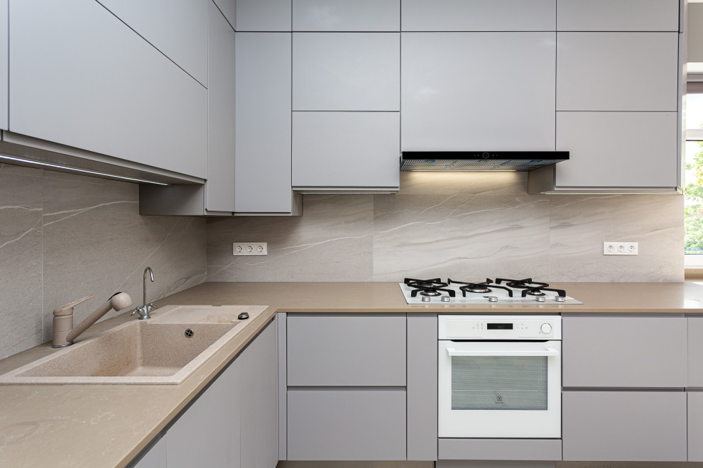 Inspiration for a mid-sized contemporary l-shaped eat-in kitchen with an undermount sink, flat-panel cabinets, grey cabinets, quartz benchtops, grey splashback, porcelain splashback, white appliances, laminate floors, no island, beige floor and beige benchtop.