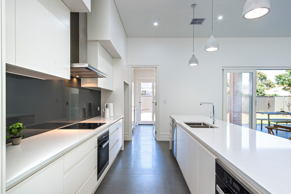 Design ideas for a large modern galley open plan kitchen in Adelaide with an undermount sink, flat-panel cabinets, white cabinets, quartz benchtops, grey splashback, glass sheet splashback, black appliances, porcelain floors, with island, grey floor and white benchtop.