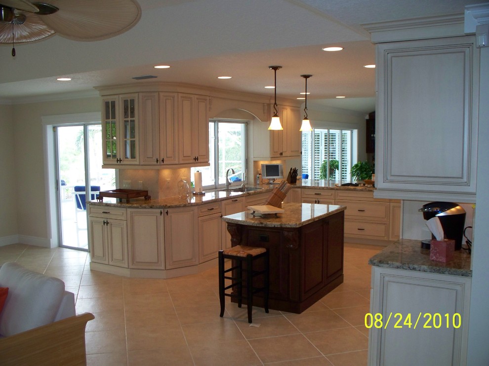Photo of a large traditional u-shaped open plan kitchen in Miami with an undermount sink, louvered cabinets, white cabinets, granite benchtops, beige splashback, ceramic splashback, stainless steel appliances, ceramic floors and with island.