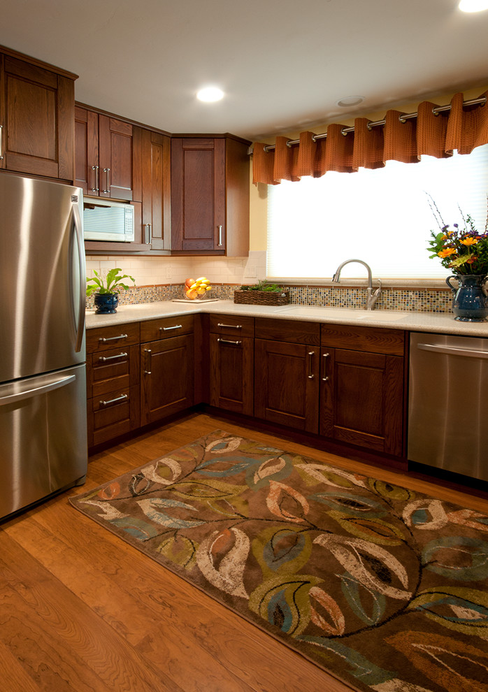 Inspiration for a mid-sized transitional u-shaped medium tone wood floor eat-in kitchen remodel in San Diego with an integrated sink, medium tone wood cabinets, solid surface countertops, stainless steel appliances, raised-panel cabinets, multicolored backsplash, mosaic tile backsplash and a peninsula