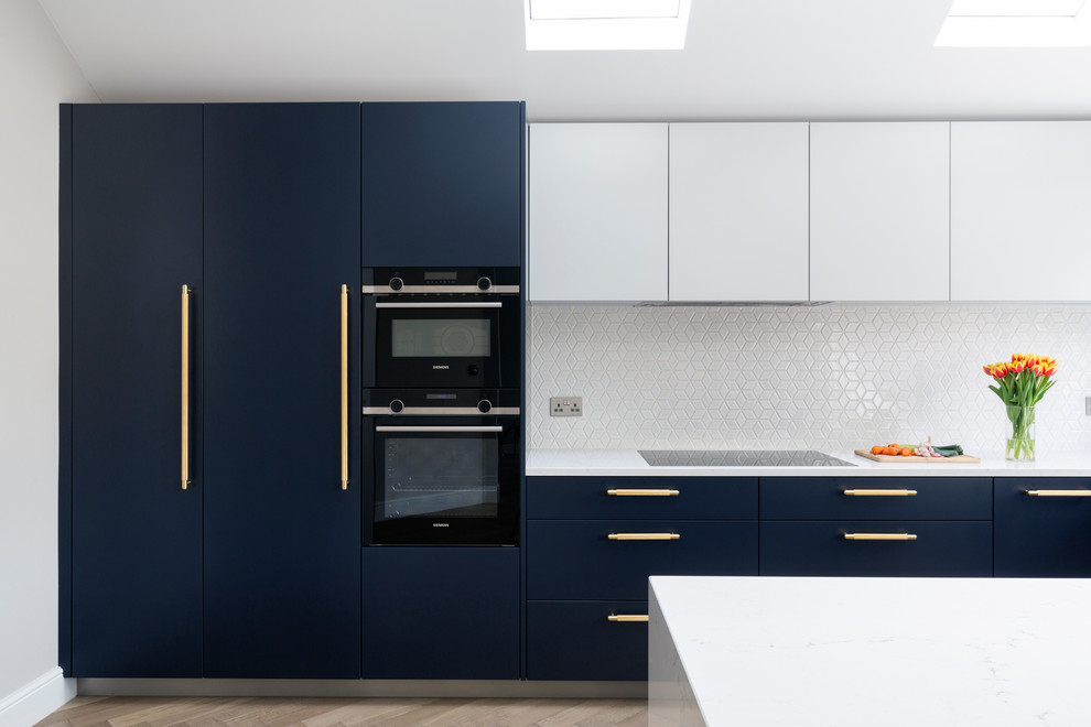 This is an example of a mid-sized u-shaped open plan kitchen in London with an integrated sink, marble benchtops, white splashback, ceramic splashback, black appliances, light hardwood floors, a peninsula, brown floor and white benchtop.