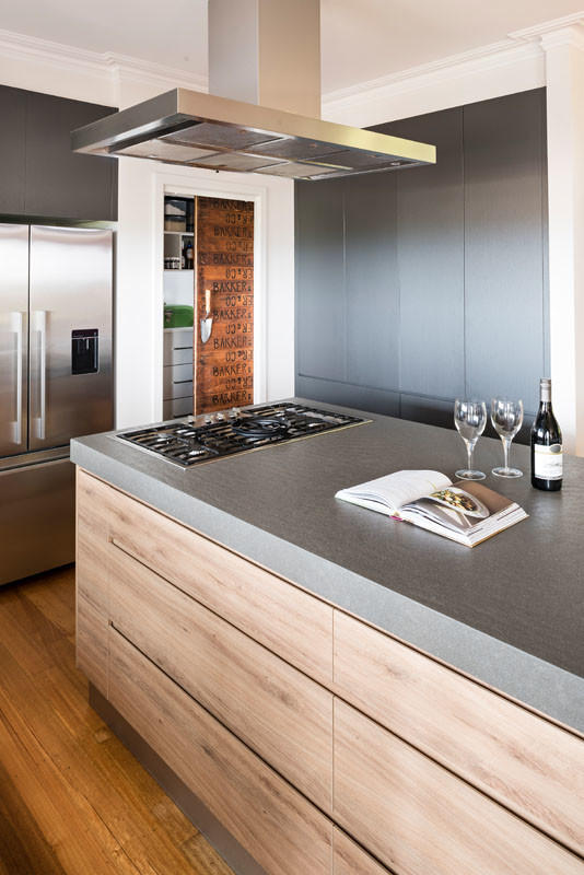 This is an example of a large industrial l-shaped open plan kitchen in Melbourne with an undermount sink, flat-panel cabinets, light wood cabinets, concrete benchtops, metallic splashback, black appliances, medium hardwood floors and with island.