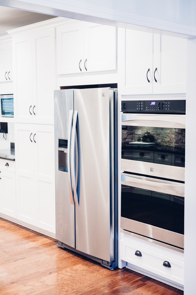 Inspiration for a large transitional galley light wood floor and brown floor open concept kitchen remodel with an undermount sink, shaker cabinets, white cabinets, quartz countertops, white backsplash, stone tile backsplash, stainless steel appliances and a peninsula