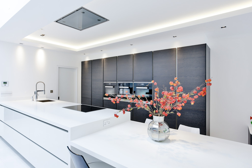 This is an example of a contemporary galley eat-in kitchen in London with flat-panel cabinets, dark wood cabinets, black appliances and with island.
