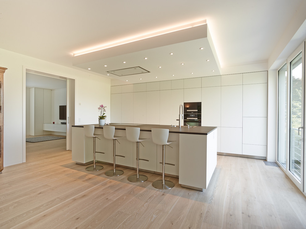 Inspiration for a large contemporary open plan kitchen in Cologne with a drop-in sink, flat-panel cabinets, white cabinets, panelled appliances, medium hardwood floors, with island and brown floor.