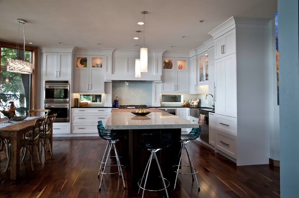 Inspiration for a large transitional l-shaped eat-in kitchen in Other with a farmhouse sink, shaker cabinets, white cabinets, quartzite benchtops, glass sheet splashback, stainless steel appliances, medium hardwood floors, with island, brown floor and blue splashback.