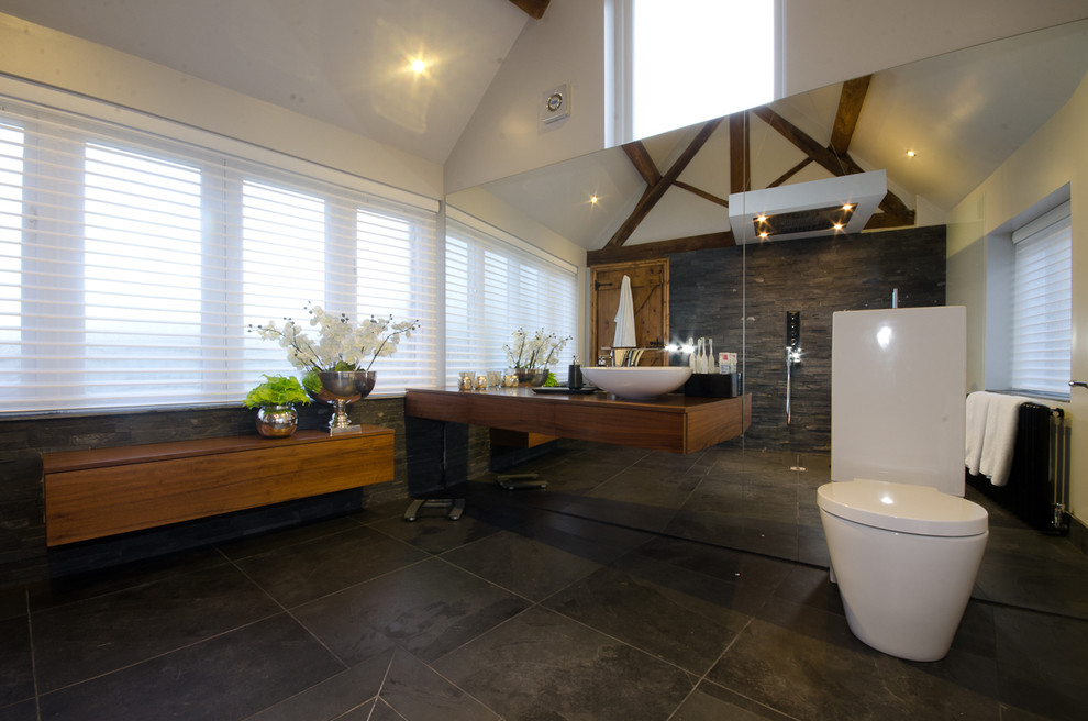 Photo of a contemporary bathroom in West Midlands with flat-panel cabinets, medium wood cabinets, wood benchtops, an open shower, a one-piece toilet, gray tile, stone tile, white walls and slate floors.