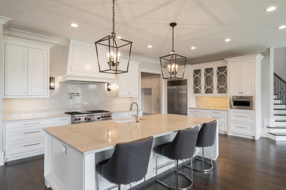 Large country l-shaped open plan kitchen in Atlanta with an undermount sink, recessed-panel cabinets, white cabinets, quartz benchtops, beige splashback, stone slab splashback, stainless steel appliances, dark hardwood floors, with island, brown floor and beige benchtop.