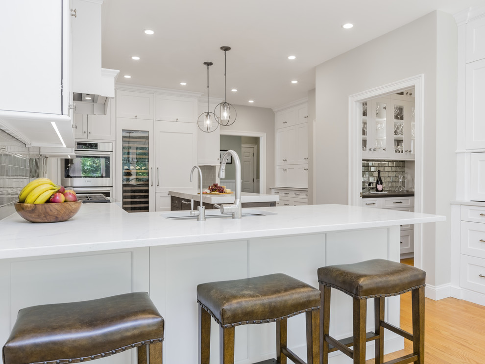Inspiration for a transitional u-shaped eat-in kitchen remodel in Providence with an undermount sink, white cabinets, quartzite countertops, glass tile backsplash, stainless steel appliances and an island