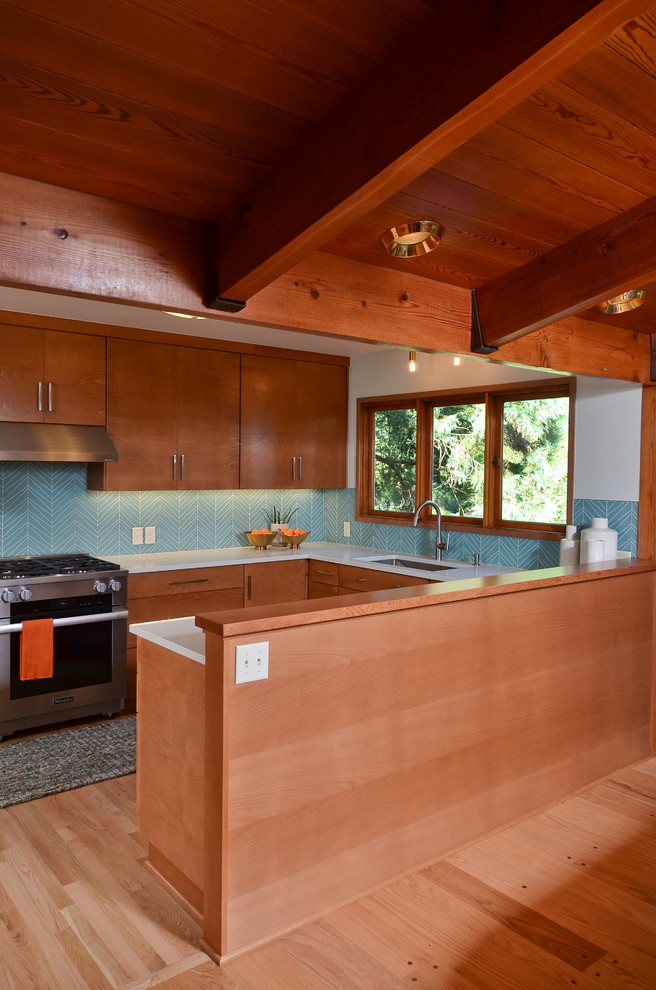 Design ideas for a mid-sized midcentury u-shaped eat-in kitchen in Portland with an undermount sink, flat-panel cabinets, medium wood cabinets, quartz benchtops, blue splashback, glass tile splashback, stainless steel appliances, light hardwood floors, a peninsula and white benchtop.