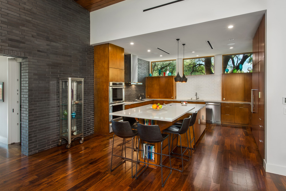 This is an example of a mid-sized midcentury u-shaped open plan kitchen in Dallas with an undermount sink, flat-panel cabinets, medium wood cabinets, quartz benchtops, white splashback, ceramic splashback, stainless steel appliances, medium hardwood floors, multiple islands, brown floor and white benchtop.