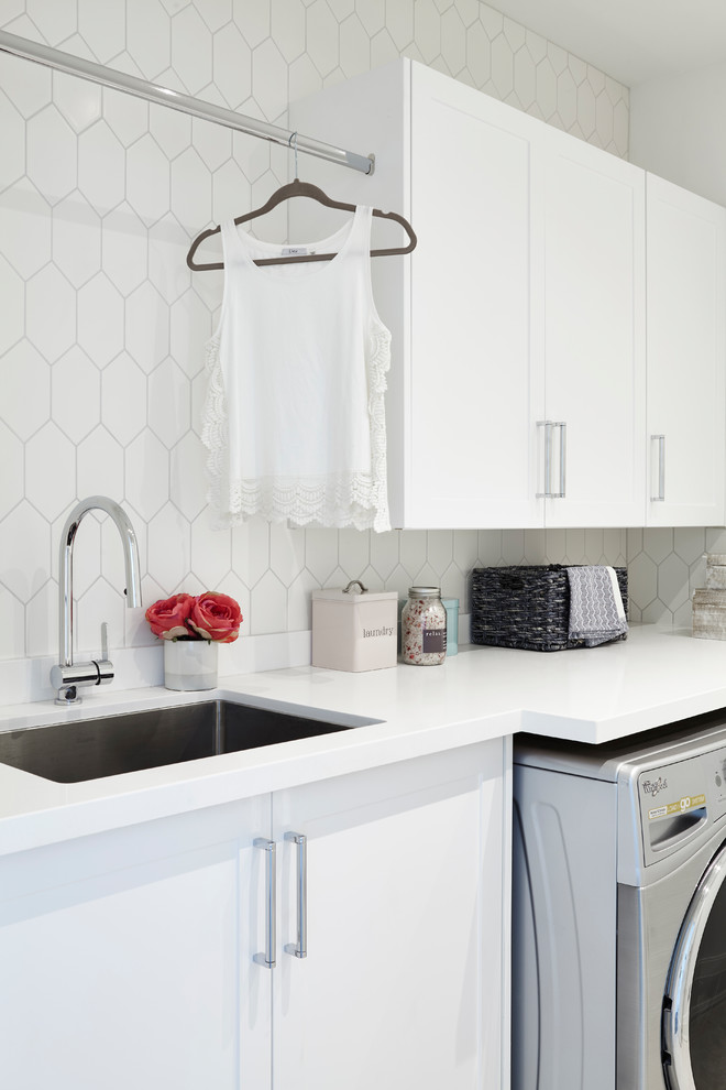 This is an example of a mid-sized transitional single-wall dedicated laundry room in Toronto with an undermount sink, shaker cabinets, white cabinets, quartz benchtops, white walls, porcelain floors, a side-by-side washer and dryer, beige floor and white benchtop.