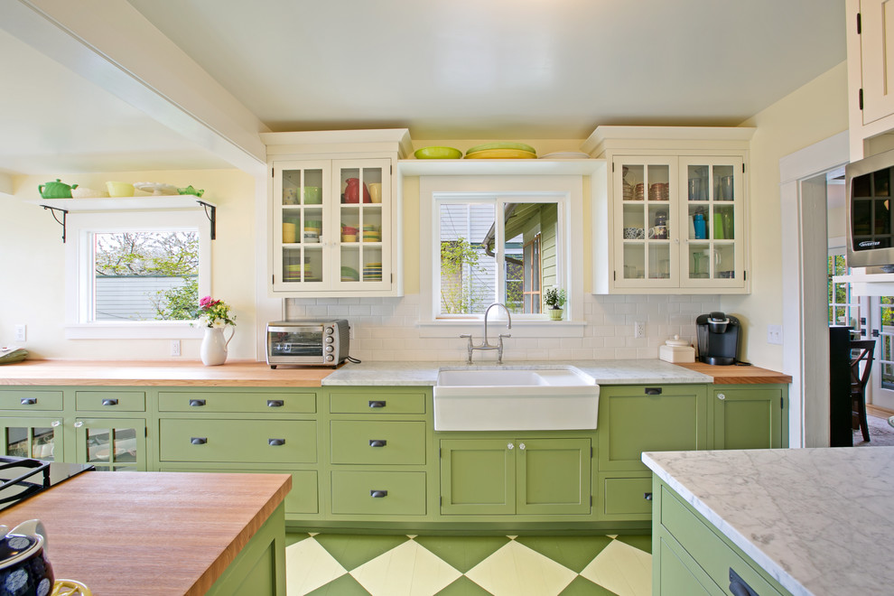 This is an example of an arts and crafts u-shaped separate kitchen in Seattle with a farmhouse sink, glass-front cabinets, green cabinets, wood benchtops, white splashback, subway tile splashback, stainless steel appliances, painted wood floors and with island.