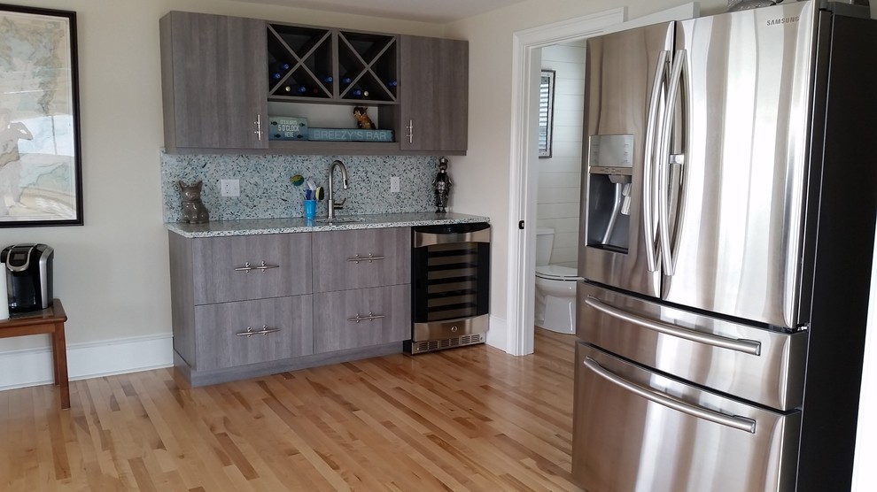 This is an example of a large beach style single-wall wet bar in Boston with an undermount sink, flat-panel cabinets, grey cabinets, recycled glass benchtops, blue splashback and light hardwood floors.