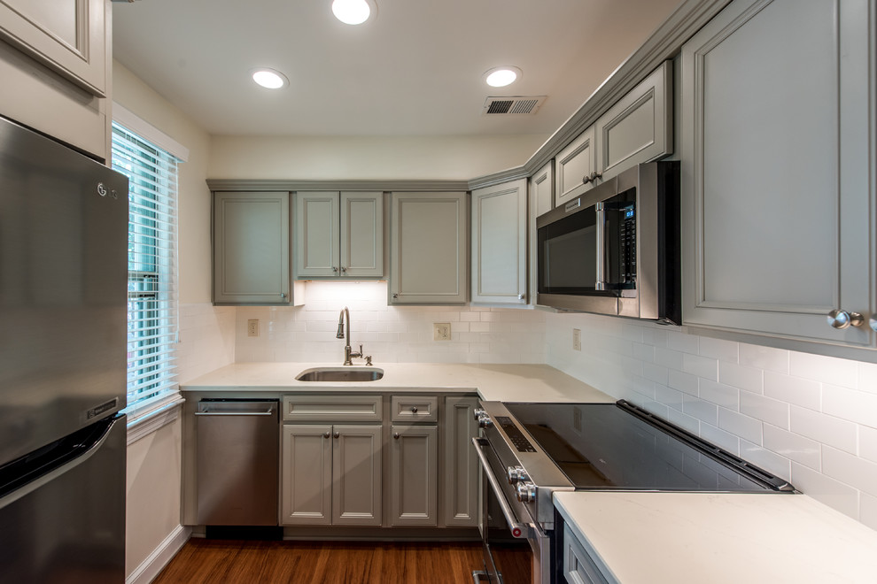 Small transitional l-shaped eat-in kitchen in DC Metro with an undermount sink, shaker cabinets, grey cabinets, quartz benchtops, white splashback, porcelain splashback, stainless steel appliances, vinyl floors, no island and brown floor.