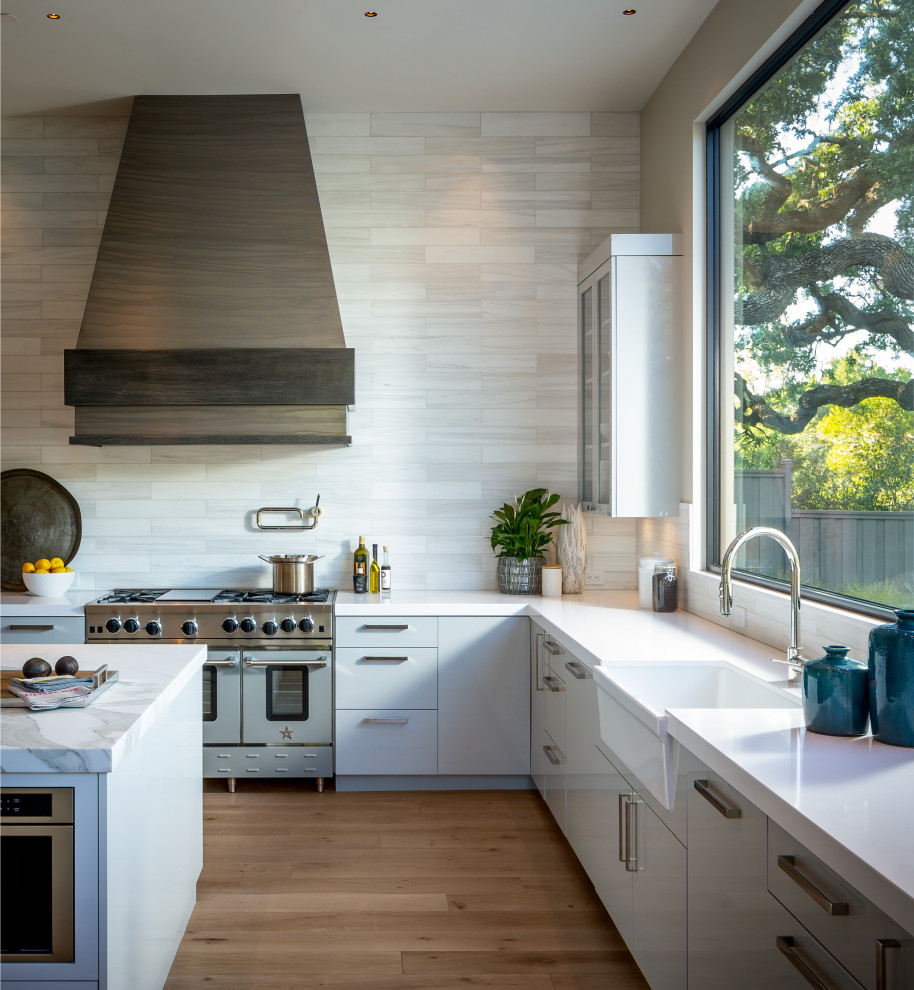 Design ideas for an expansive contemporary l-shaped kitchen in San Francisco with a farmhouse sink, flat-panel cabinets, grey cabinets, beige splashback, coloured appliances, medium hardwood floors, with island, brown floor and white benchtop.