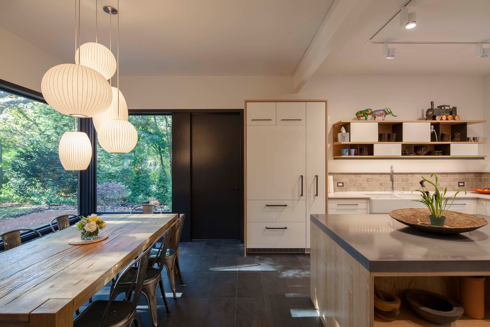 Design ideas for a contemporary l-shaped eat-in kitchen in Boston with a farmhouse sink, flat-panel cabinets, white cabinets, grey splashback, panelled appliances, concrete benchtops, slate floors, with island, black floor and white benchtop.