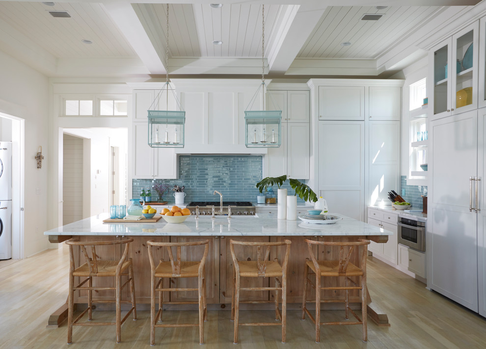 Inspiration for a beach style l-shaped kitchen in Other with recessed-panel cabinets, white cabinets, blue splashback, stainless steel appliances, light hardwood floors, with island, beige floor and white benchtop.
