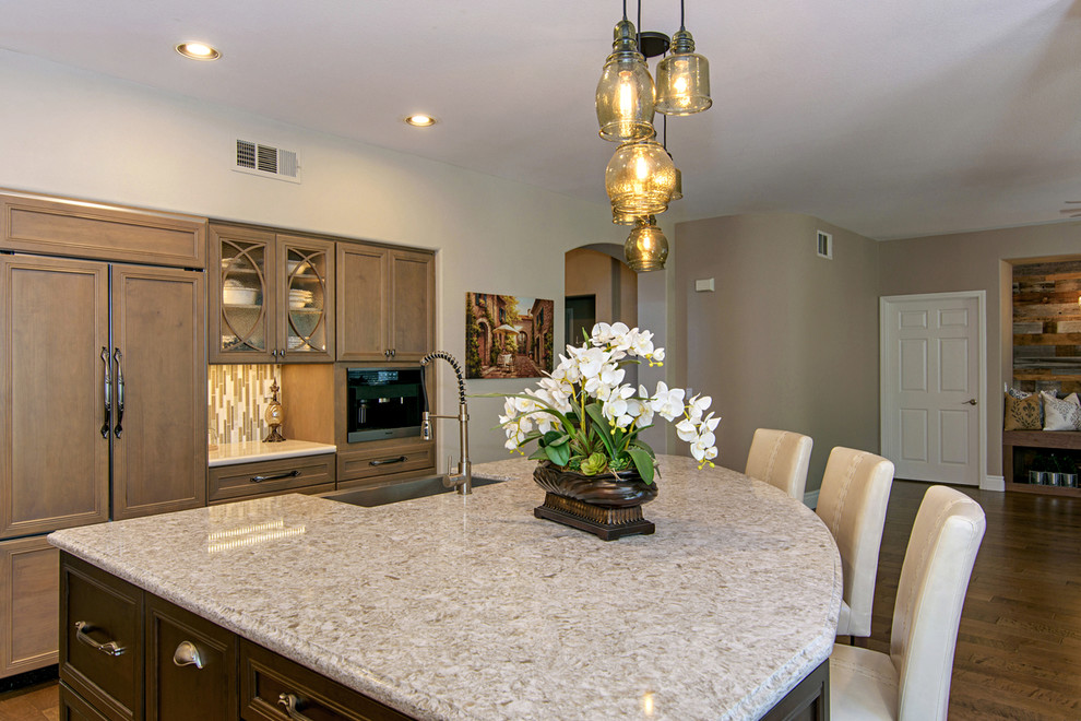 Large transitional l-shaped medium tone wood floor and brown floor open concept kitchen photo in San Diego with a farmhouse sink, recessed-panel cabinets, medium tone wood cabinets, beige backsplash, paneled appliances, an island, quartz countertops and travertine backsplash