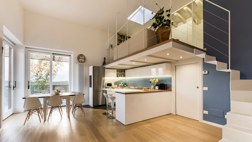 Photo of a large scandinavian u-shaped eat-in kitchen in Milan with a drop-in sink, flat-panel cabinets, white cabinets, wood benchtops, blue splashback, stainless steel appliances, porcelain floors, multiple islands and grey floor.