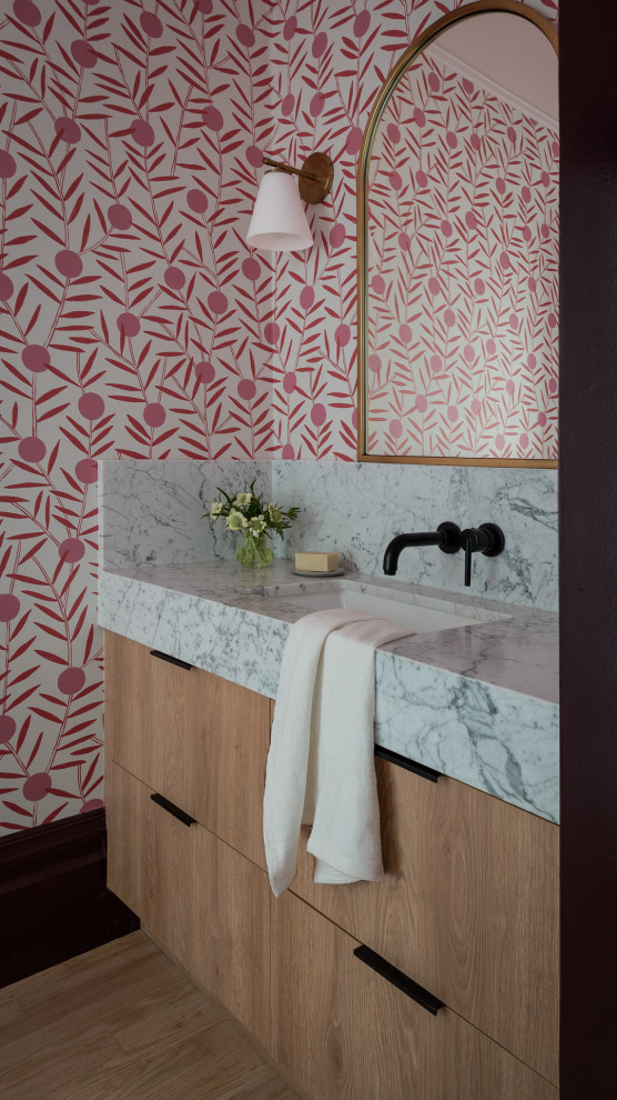 Powder room - contemporary medium tone wood floor, brown floor and wallpaper powder room idea in San Francisco with flat-panel cabinets, light wood cabinets, pink walls, an undermount sink, marble countertops, white countertops and a built-in vanity