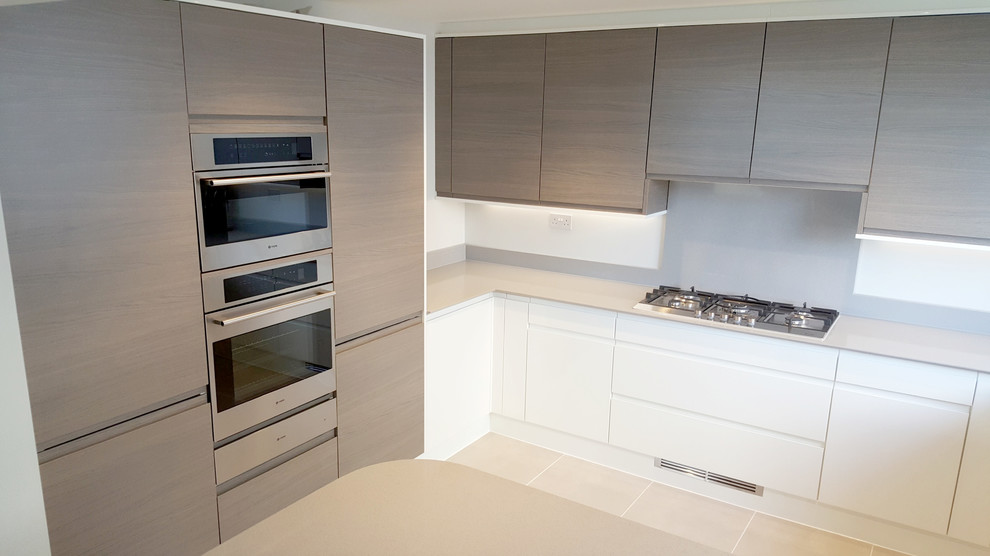 Bild på ett mellanstort funkis kök, med en integrerad diskho, släta luckor, vita skåp, bänkskiva i kvartsit, grått stänkskydd, stänkskydd i sten, rostfria vitvaror, klinkergolv i keramik och en halv köksö