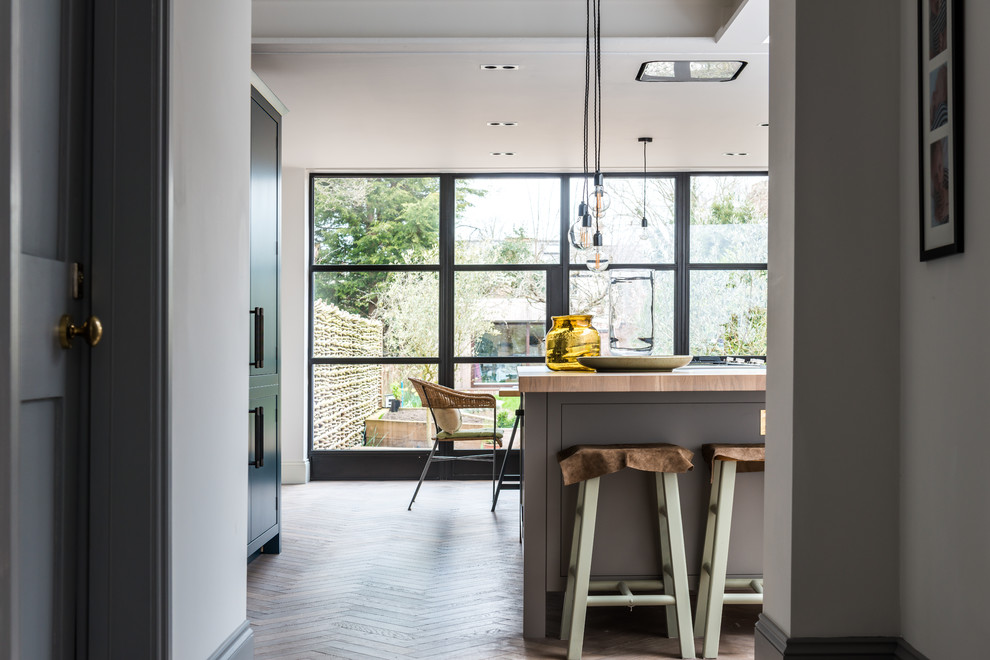 Design ideas for a large contemporary u-shaped eat-in kitchen in Oxfordshire with an undermount sink, flat-panel cabinets, grey cabinets, solid surface benchtops, white splashback, marble splashback, stainless steel appliances, light hardwood floors and with island.