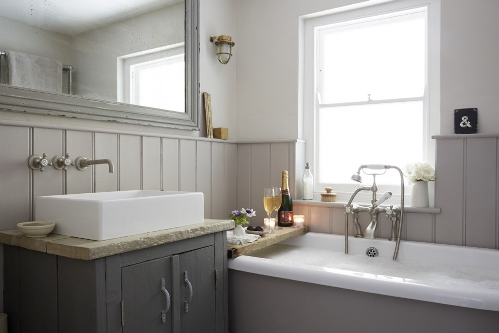 Inspiration for a mid-sized country kids bathroom in Cornwall with shaker cabinets, grey cabinets, a drop-in tub, a shower/bathtub combo, a one-piece toilet, white tile, white walls, painted wood floors, a trough sink and white floor.
