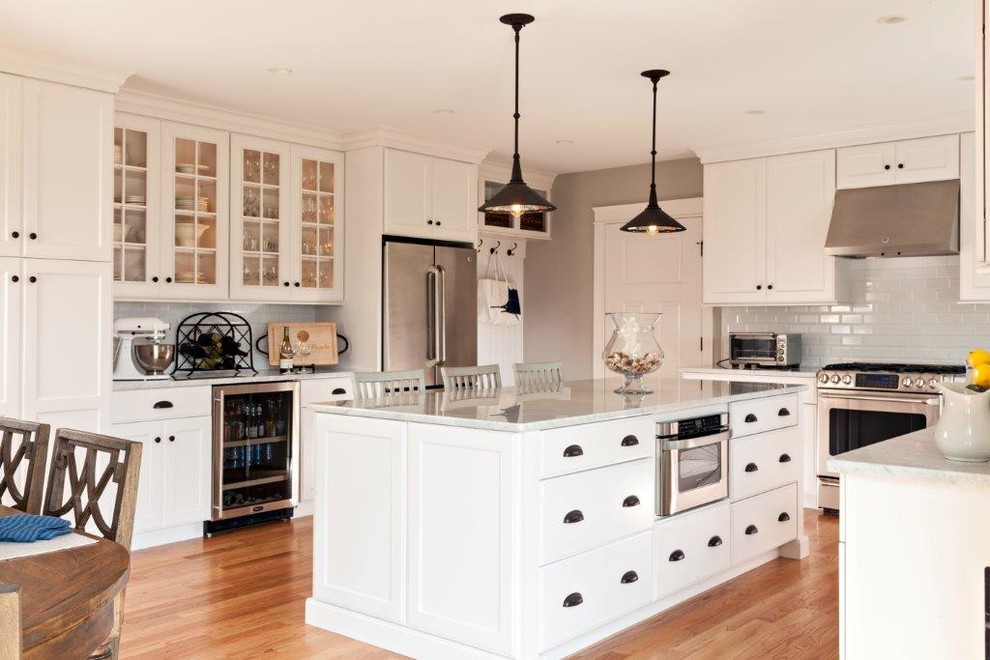Mid-sized transitional l-shaped light wood floor and beige floor eat-in kitchen photo in Boston with recessed-panel cabinets, white cabinets, granite countertops, white backsplash, subway tile backsplash, stainless steel appliances, an island and a farmhouse sink