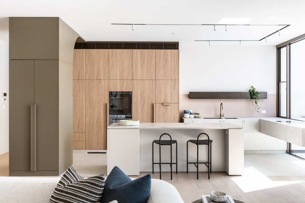 Moderne Küche in L-Form mit flächenbündigen Schrankfronten, hellen Holzschränken, Küchenrückwand in Rosa, schwarzen Elektrogeräten, Kücheninsel, weißer Arbeitsplatte, Unterbauwaschbecken, hellem Holzboden und beigem Boden in Melbourne