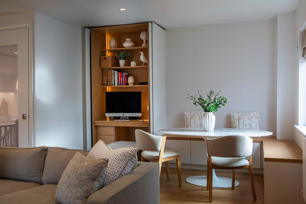 Photo of a small contemporary study in Dublin with white walls, light hardwood flooring and a built-in desk.