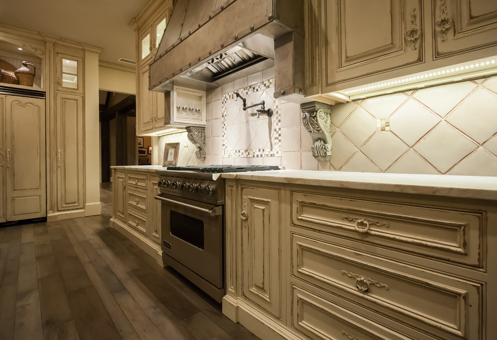 Example of a huge mountain style u-shaped light wood floor eat-in kitchen design with raised-panel cabinets, distressed cabinets, beige backsplash, stainless steel appliances, an island, an undermount sink, marble countertops and ceramic backsplash