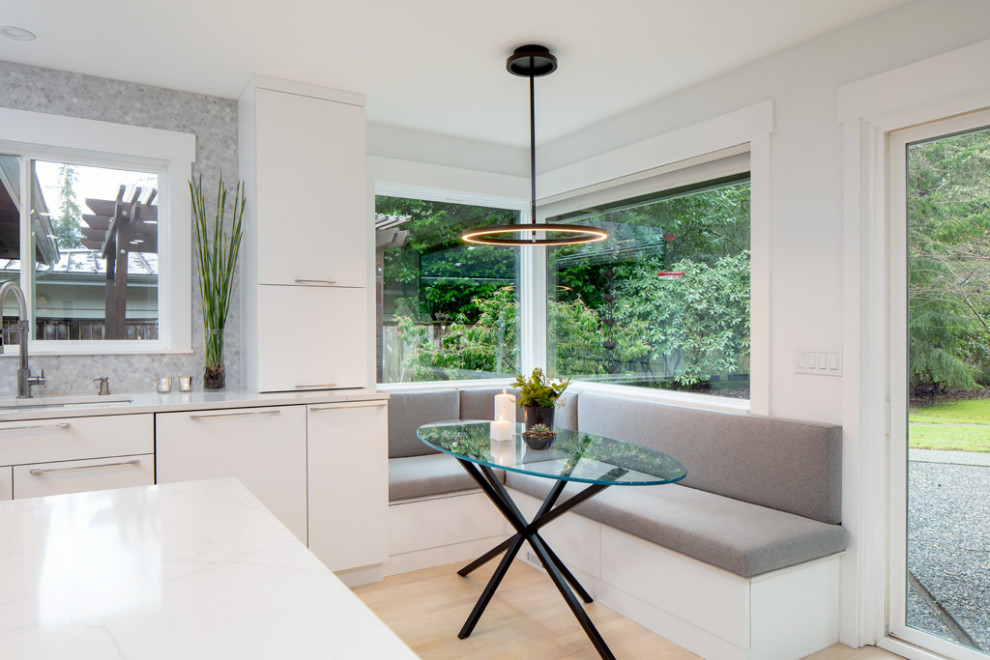 Mid-sized contemporary single-wall eat-in kitchen in Seattle with an undermount sink, flat-panel cabinets, white cabinets, quartz benchtops, grey splashback, porcelain splashback, white appliances, light hardwood floors, with island and white benchtop.