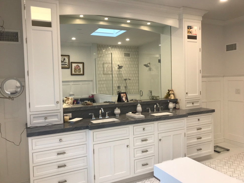 This is an example of a large transitional master bathroom in New York with recessed-panel cabinets, white cabinets, a corner shower, a bidet, white tile, marble, white walls, marble floors, an undermount sink, engineered quartz benchtops, white floor, a hinged shower door, black benchtops, a double vanity, a built-in vanity and panelled walls.