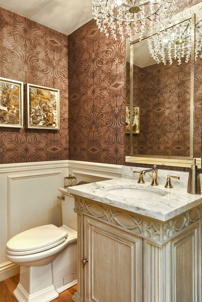 Photo of a small traditional powder room in San Francisco with recessed-panel cabinets, grey cabinets, a two-piece toilet, brown walls, light hardwood floors, an undermount sink, marble benchtops, brown floor, grey benchtops, a freestanding vanity and wallpaper.