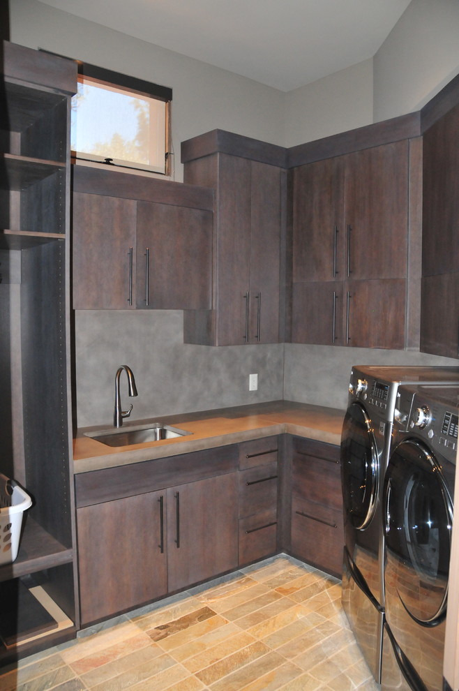 Mid-sized transitional l-shaped dedicated laundry room in Phoenix with concrete benchtops, an undermount sink, flat-panel cabinets, dark wood cabinets, grey walls, slate floors, a side-by-side washer and dryer, multi-coloured floor and grey benchtop.