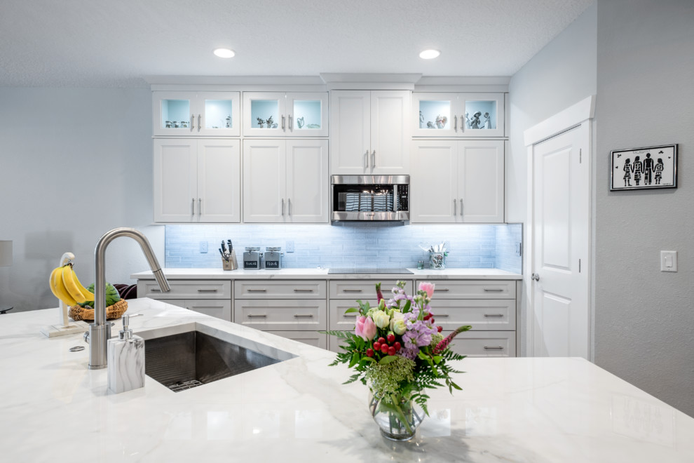 Inspiration for a mid-sized transitional l-shaped eat-in kitchen in Tampa with an undermount sink, shaker cabinets, white cabinets, tile benchtops, grey splashback, subway tile splashback, black appliances, medium hardwood floors, with island, brown floor and white benchtop.