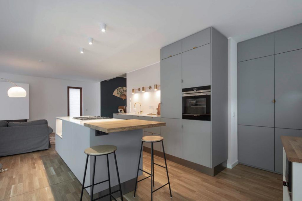Photo of a mid-sized scandinavian galley eat-in kitchen in Other with an undermount sink, flat-panel cabinets, grey cabinets, pink splashback, black appliances, light hardwood floors, with island and white benchtop.