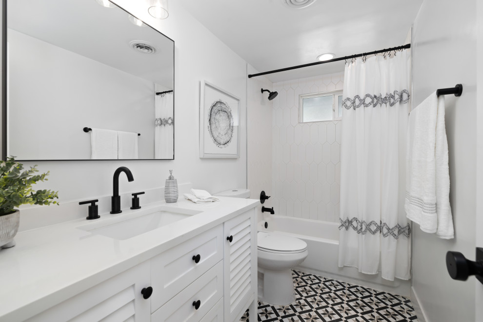 Foto på ett mellanstort 60 tals vit badrum med dusch, med luckor med lamellpanel, vita skåp, ett badkar i en alkov, en toalettstol med separat cisternkåpa, vita väggar, cementgolv, ett undermonterad handfat, bänkskiva i kvarts, flerfärgat golv och dusch med duschdraperi