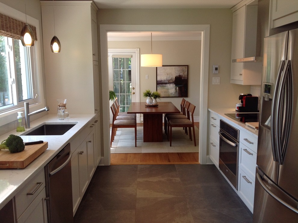 This is an example of a mid-sized transitional galley separate kitchen in Montreal with an undermount sink, shaker cabinets, white cabinets, quartz benchtops, grey splashback, subway tile splashback, stainless steel appliances, porcelain floors and no island.